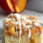 Titled Pinterest image of a slice of Peach Coffee Cake on a gray plate, with a peach cut open in the background.