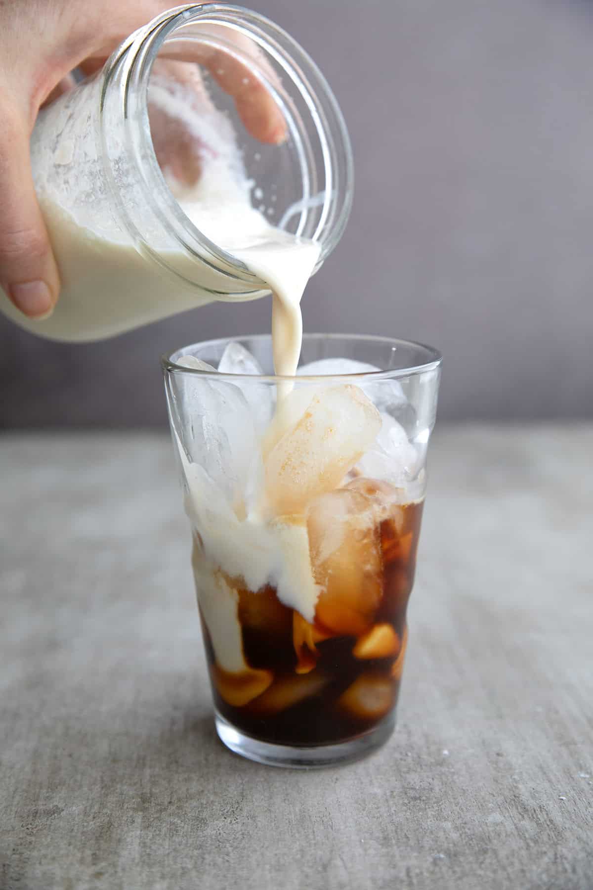 A jar of protein milk being poured into a glass with ice and espresso.