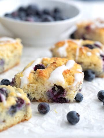 Keto Blueberry Biscuits on a piece of white parchment paper with a bowl of blueberries in the background.