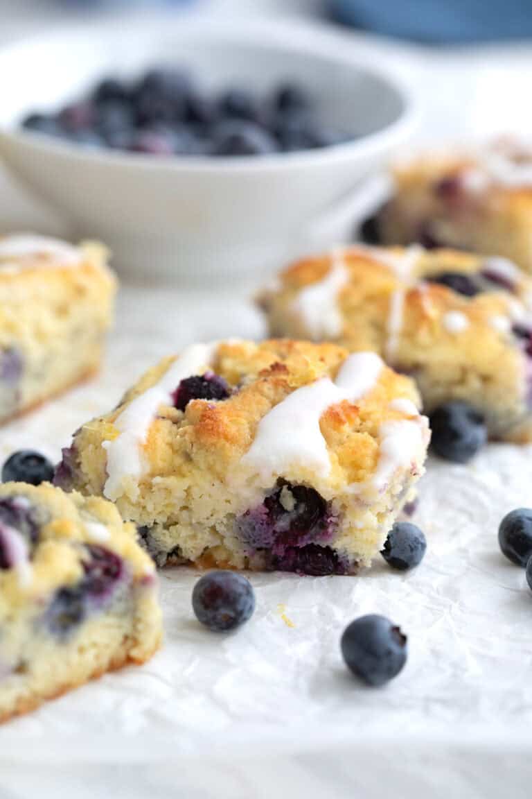 Keto Blueberry Biscuits on a piece of white parchment paper with a bowl of blueberries in the background.