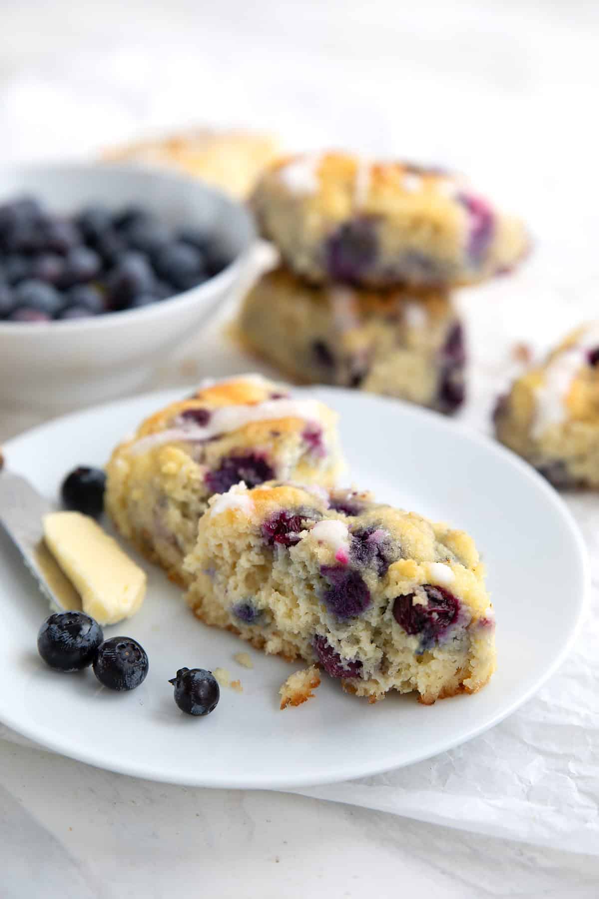 A Keto Blueberry Biscuits broken open on a white plate, with a knife with butter on it.