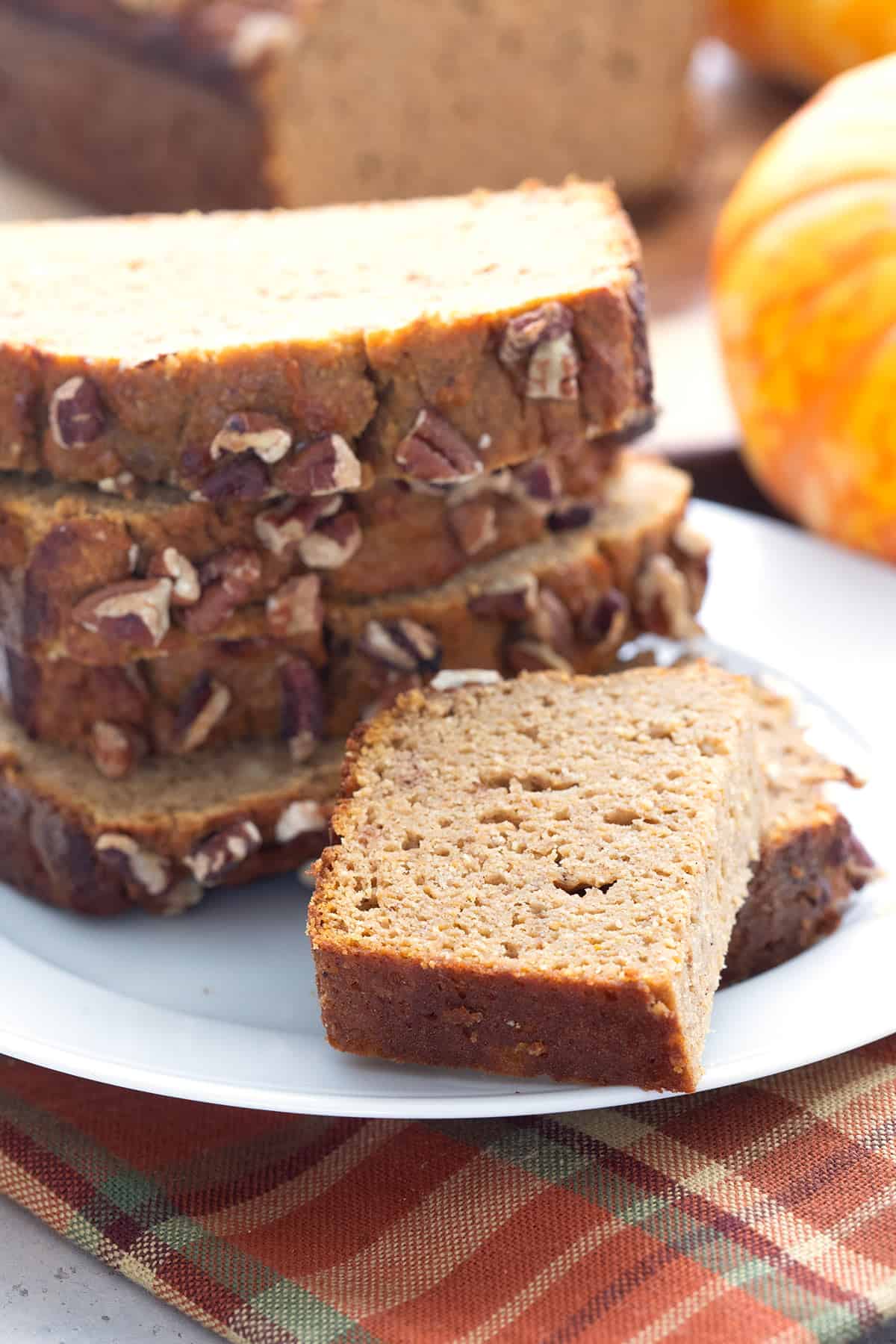 Slices of coconut flour pumpkin bread piled up on a white plate.