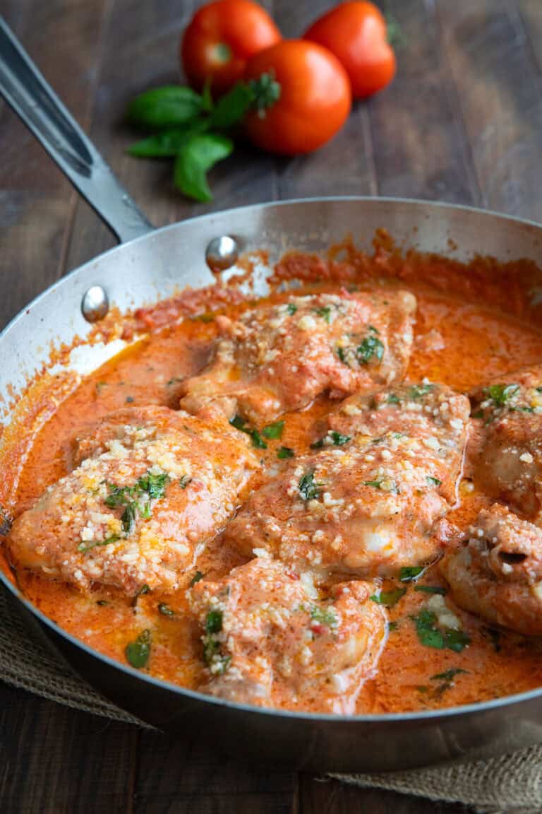 Tomato basil chicken in a skillet on a wooden table, with tomatoes and basil in the background.