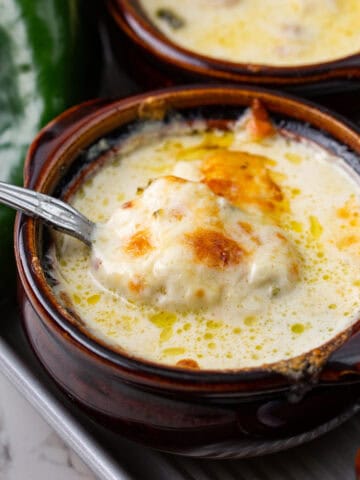 Close up shot of a spoon digging into the broiled cheese topping on a bowl of Chile Relleno Soup.