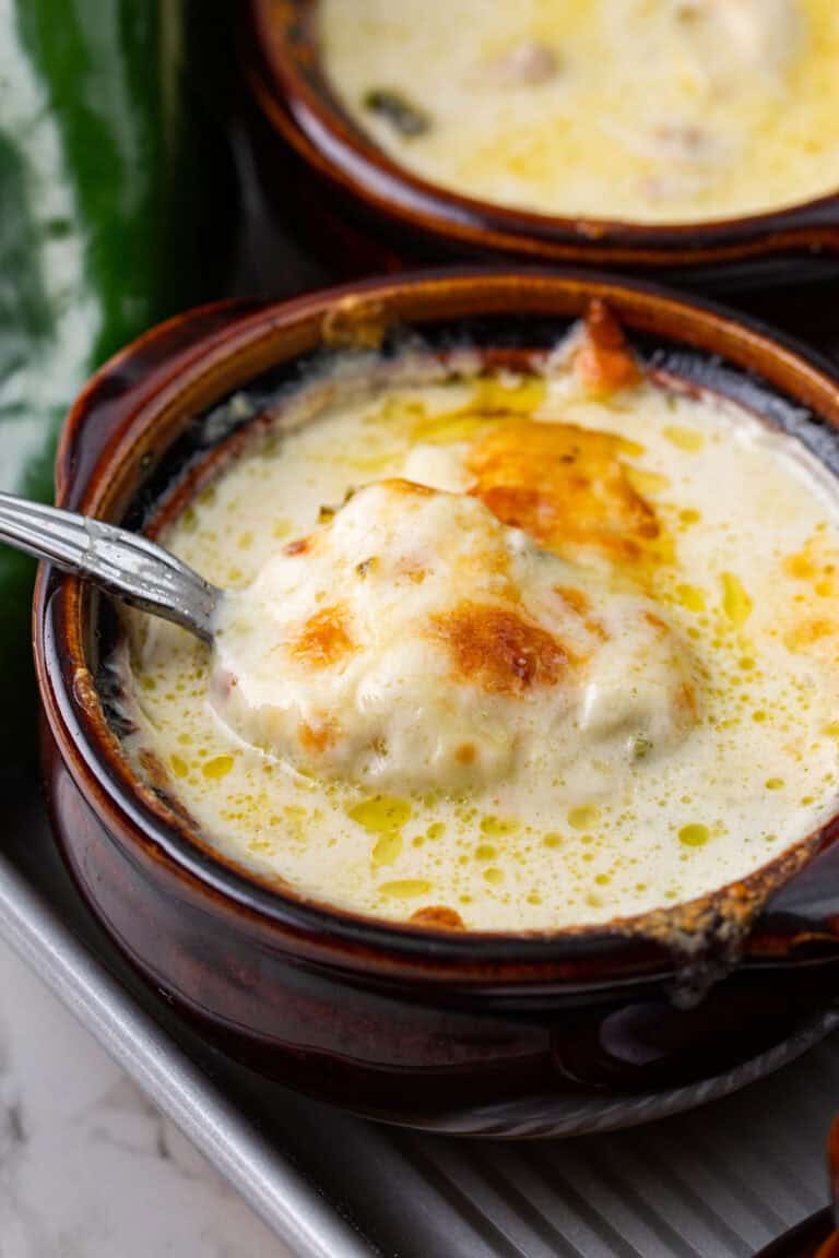 Close up shot of a spoon digging into the broiled cheese topping on a bowl of Chile Relleno Soup.