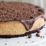 Titled image of Keto Coffee Cheesecake on a white cake stand with chocolate glaze on top.