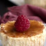 Titled image of a mini creme brûlée cheesecake on a white plate with a raspberry on top.