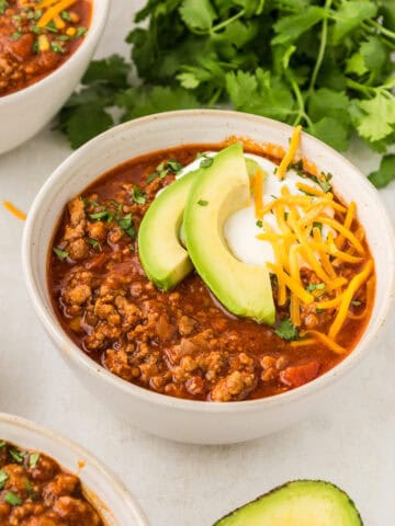 Easy keto chili in a white bowl, topped with sour cream, shredded cheddar, and avocado.