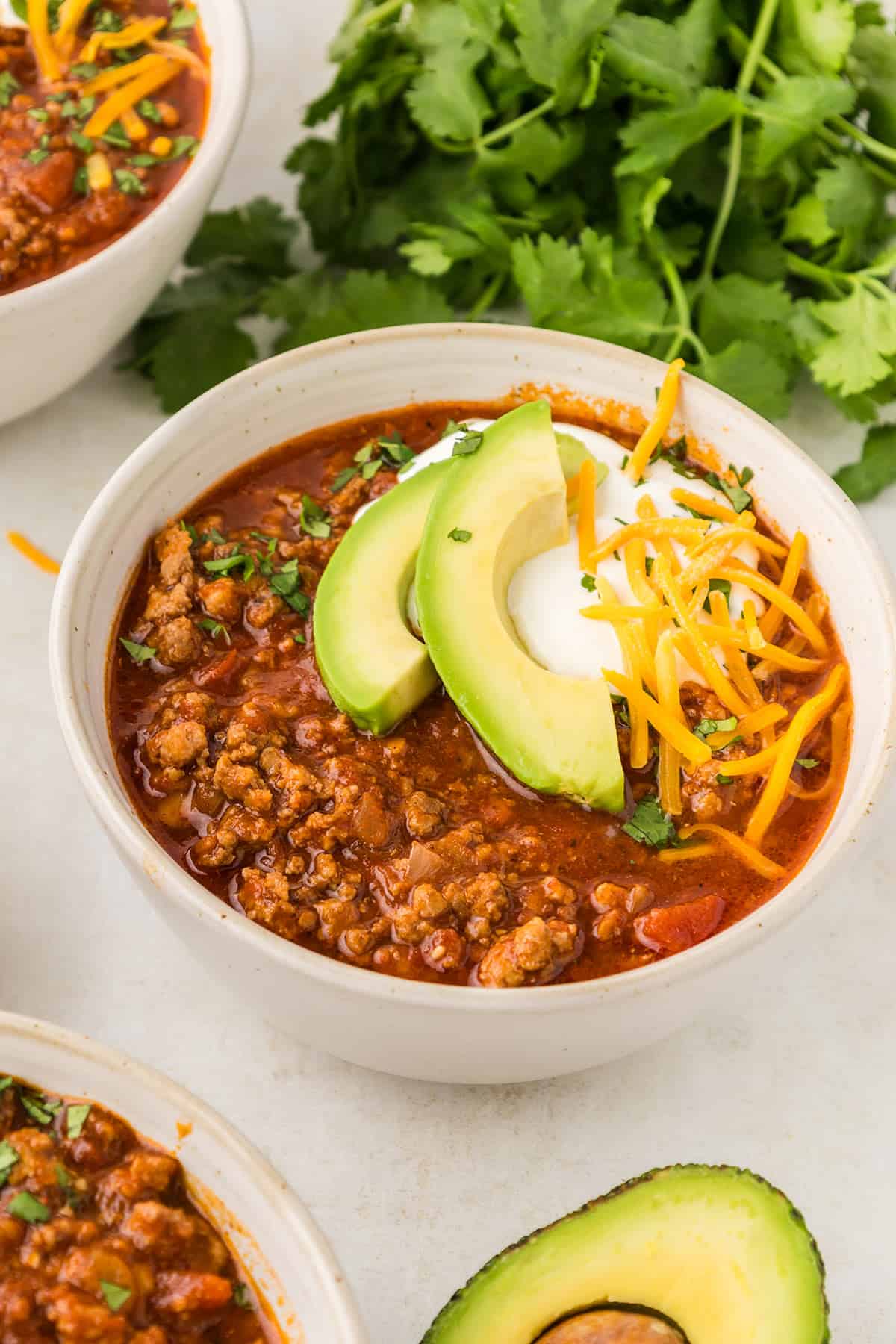 Easy keto chili in a white bowl, topped with sour cream, shredded cheddar, and avocado.