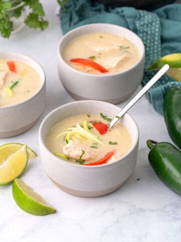 Three bowls of Keto Thai Chicken Soup on a white marble tabletop.