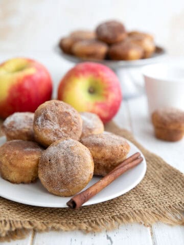 Keto Apple Cider Donut Bites on a white plate over a piece of burlap, with apples in the background.