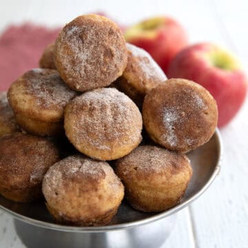 Keto Apple Cider Donut Bites stacked up on a metal cake stand on a white wooden table.