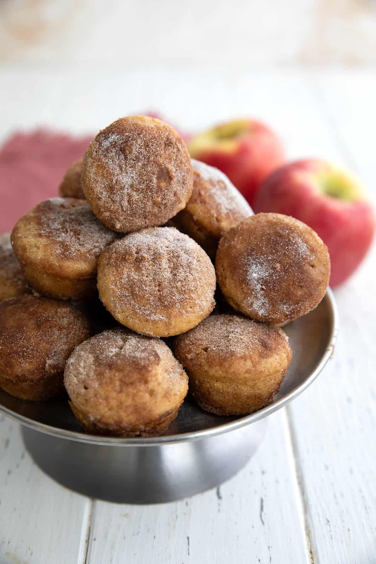 Keto Apple Cider Donut Bites stacked up on a metal cake stand on a white wooden table.