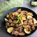 A black bowl filled with Chicken Zucchini Stir Fry on a gray concrete table.