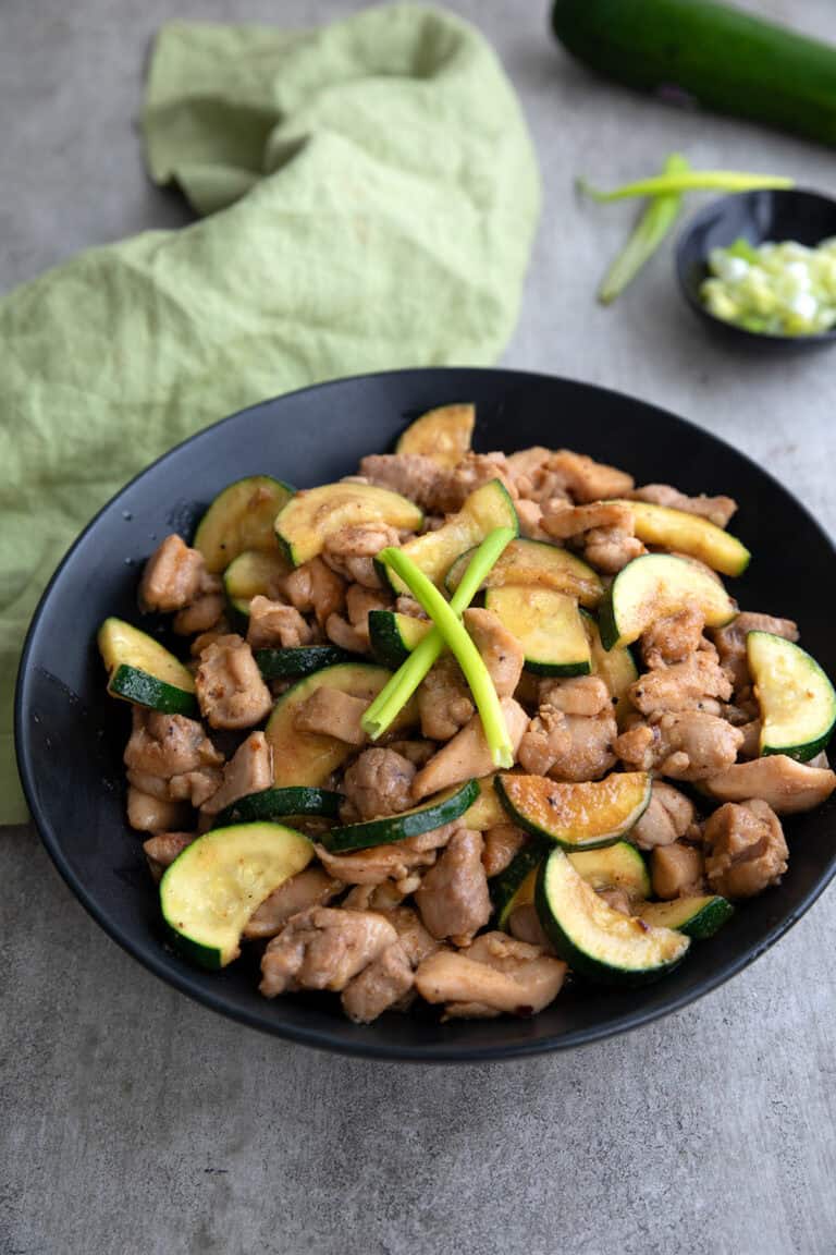 A black bowl filled with Chicken Zucchini Stir Fry on a gray concrete table.