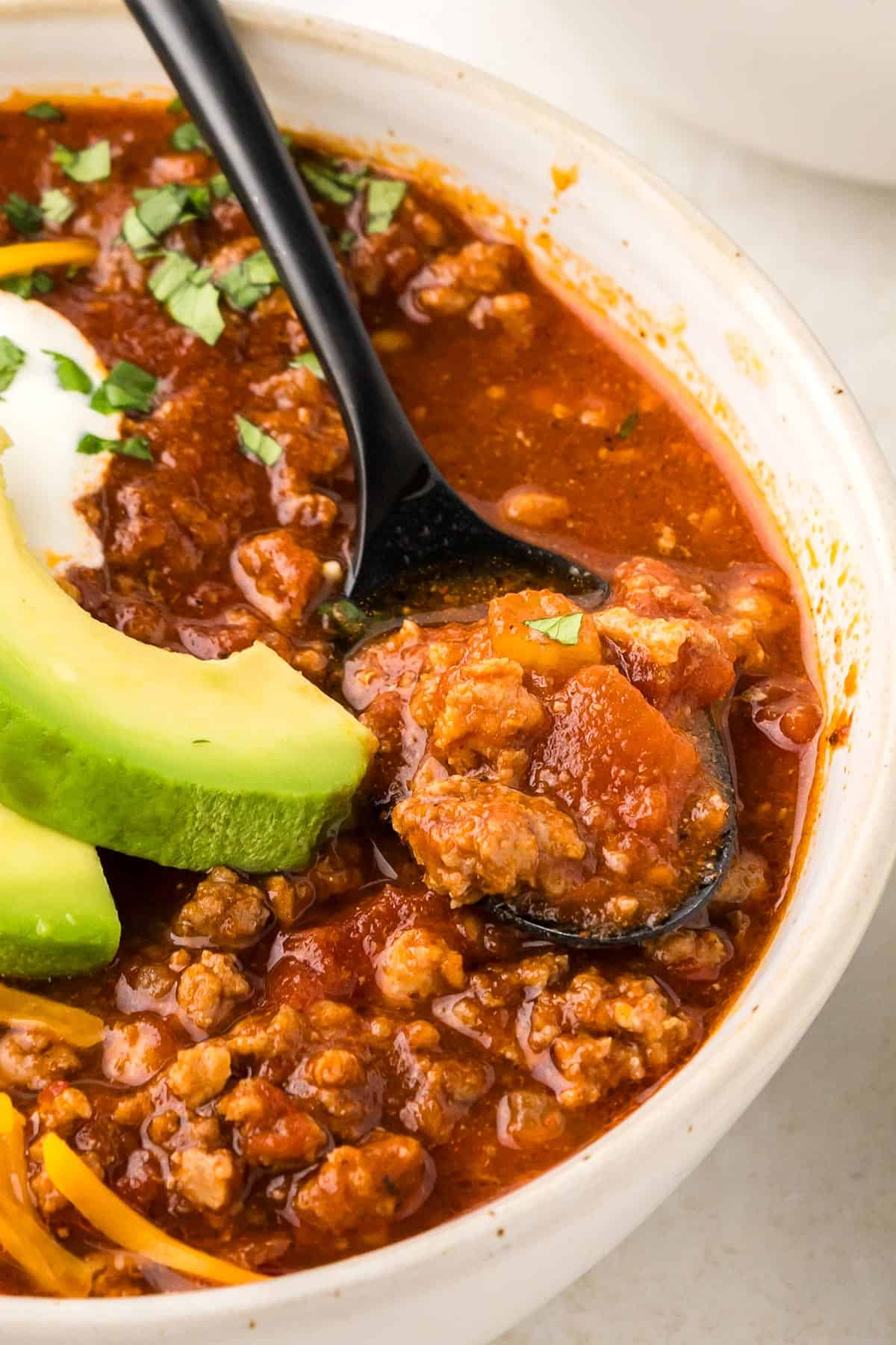 Close up shot of keto chili in a white bowl with a black spoon.