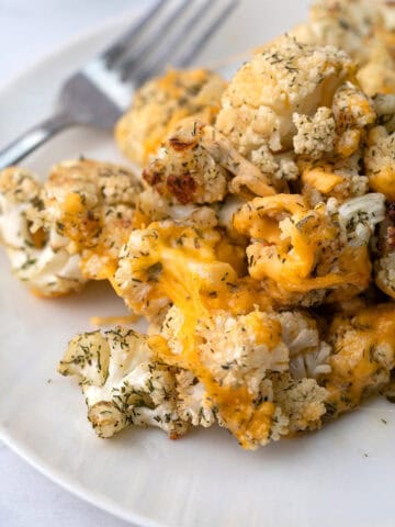 A pile of Cheddar Ranch Roasted Cauliflower on a white plate with a fork.