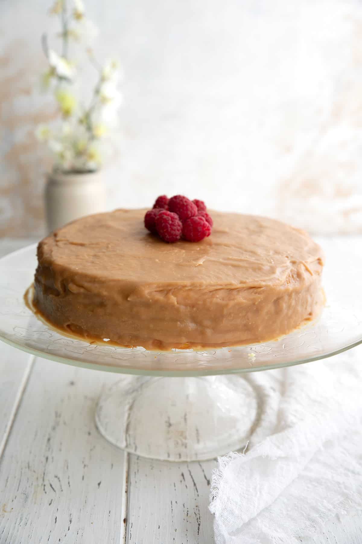 Keto Caramel Cake on a glass cake plate on a white wooden table.