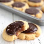 Two Keto Twix Cookies on a white wooden table with a tray of cookies in the background.