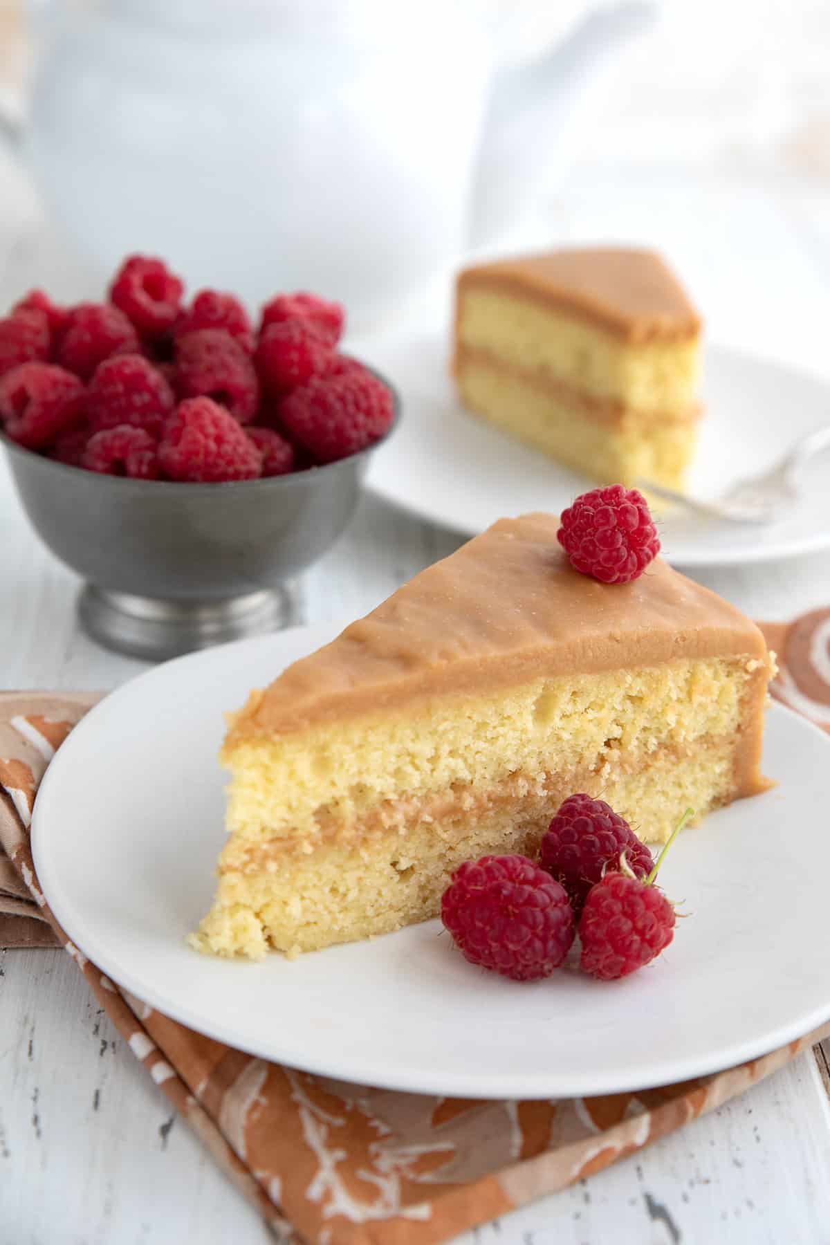 A slice of Keto Caramel Cake on a white plate with raspberries.