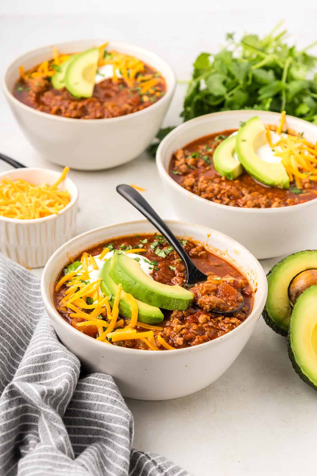 Three bowls of keto chili on a white table with a gray striped napkin.