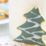 A Christmas tree shaped keto sugar cookie leaning against a glass of milk.