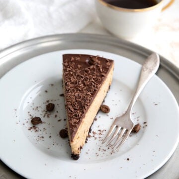 Keto Coffee Cheesecake on a white plate with a cup of coffee in the background.