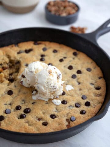 A cast iron skillet with a chocolate chip skillet cookie and ice cream on top.