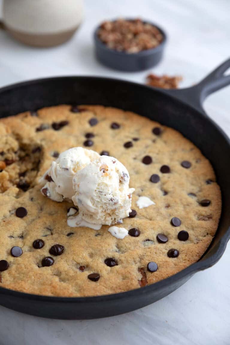 A cast iron skillet with a chocolate chip skillet cookie and ice cream on top.