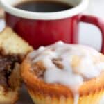 Titled image of a Cinnamon Roll Protein Muffin on a white plate with a red cup of coffee.