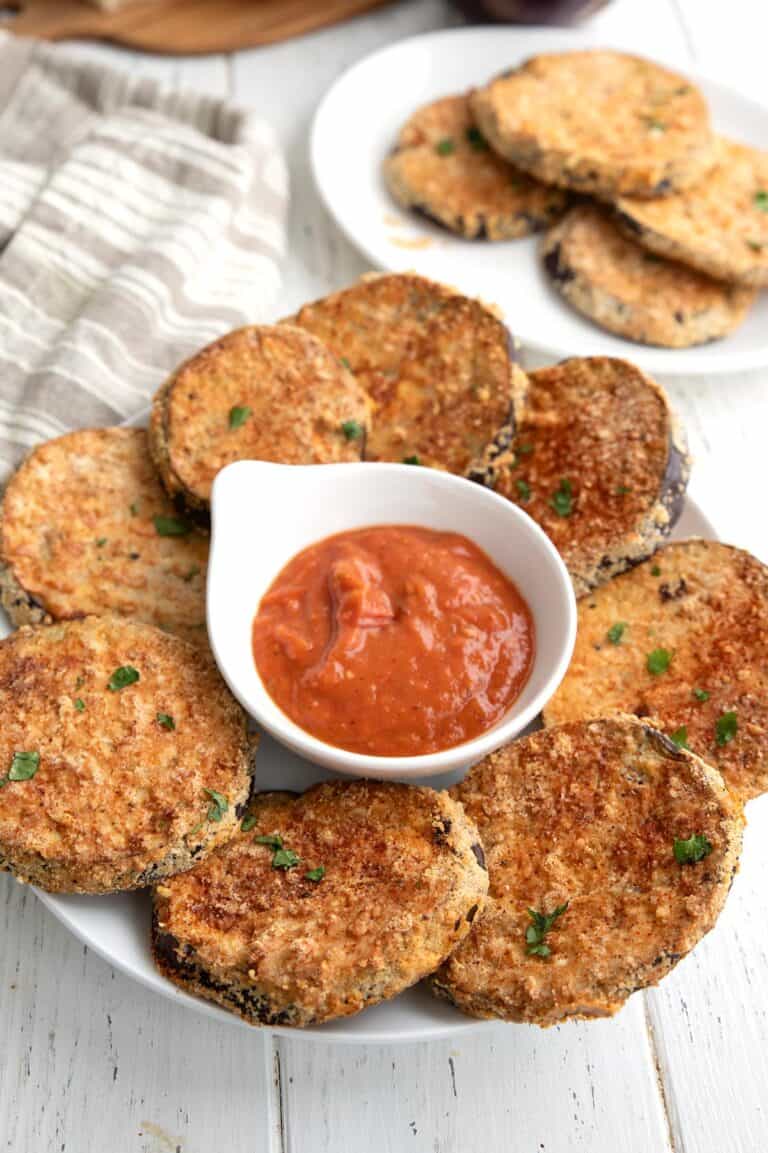 Pieces of Crispy Air Fryer Eggplant on a white plate with a bowl of marinara in the center.