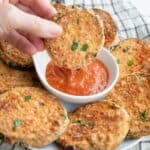 A hand dipping Crispy Air Fryer Eggplant into a small bowl of marinara sauce.