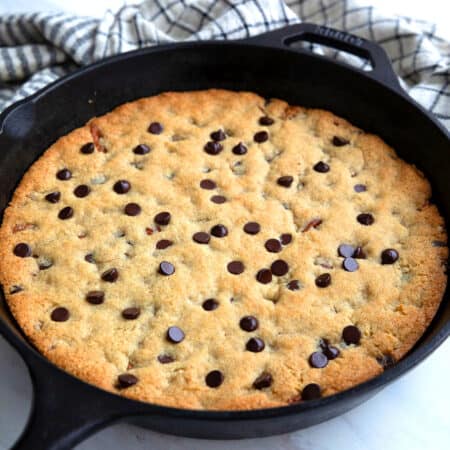 A keto chocolate chip skillet cookie in a cast iron skillet on a white table top.