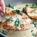 A serving spoon holding up a piece of Chicken Florentine from a skillet.