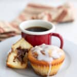 Two Cinnamon Roll Protein Muffins with a cup of coffee on a white plate.