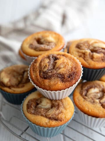 A stack of Cinnamon Roll Protein Muffins on a metal cooling rack on a white table.