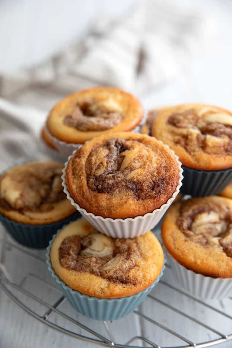 A stack of Cinnamon Roll Protein Muffins on a metal cooling rack on a white table.