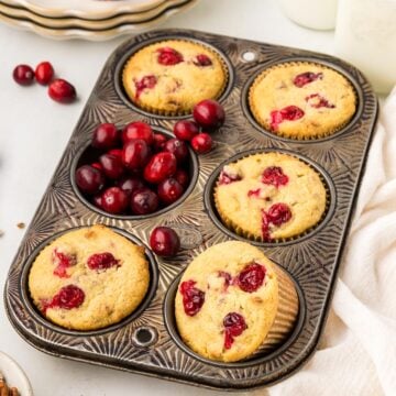 Keto Cranberry Muffins in a muffin tin with fresh cranberries filling one of the wells.