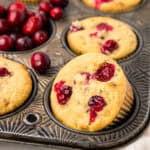 Close up shot of Keto Cranberry Muffins in a muffin tin with fresh cranberries in one of the cavities.