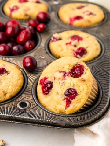 Close up shot of Keto Cranberry Muffins in a muffin tin with fresh cranberries in one of the cavities.