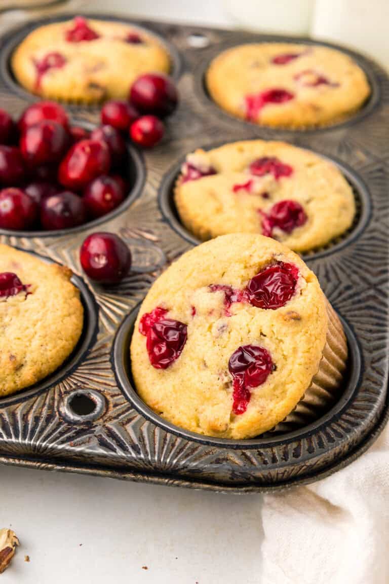 Close up shot of Keto Cranberry Muffins in a muffin tin with fresh cranberries in one of the cavities.