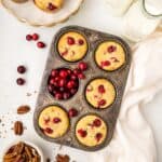 Top down image of Keto Cranberry Muffins in a muffin tin, with fresh cranberries and pecans strewn around.