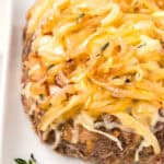 Close up shot of French Onion Meatloaf on a white platter with a sprig of fresh thyme.