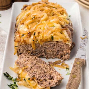 French Onion Meatloaf on a white platter with a knife, with one slice cut out.