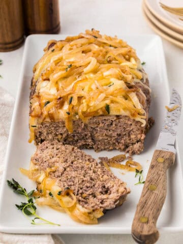 French Onion Meatloaf on a white platter with a knife, with one slice cut out.