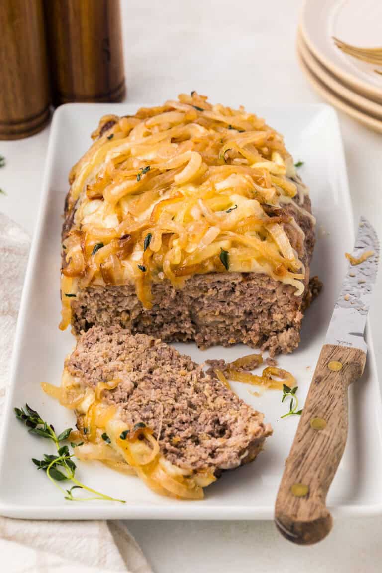 French Onion Meatloaf on a white platter with a knife, with one slice cut out.