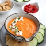 A bowl of Red Pepper Feta Dip on a gray plate with keto crackers and cucumber slices.