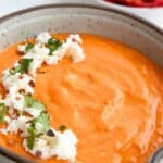 Titled image of a close up shot of Roasted Red Pepper Feta Dip in a bowl with crumbled feta on top.