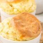 Titles image of keto cheddar chive soufflés in white ramekins on a wooden cutting board.