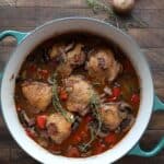 Top down image of Keto Coq au Vin in a teal dutch oven on a wooden table, with mushrooms and sprigs of thyme.